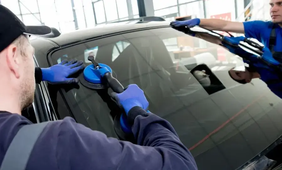 Technicians fitting a vehicle windscreen with suction tools